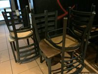 Six stacked wooden chairs with ladder-back design and round seats, showing wear and needing cleaning.