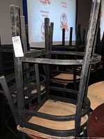 Stacked black metal chairs with wooden seats, showing wear and signs of heavy use.