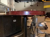 Side view of round high top table showing wood grain finish, edge and black pedestal base.