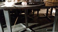 Photo showing metal tabletop and metal base, not attached, with cross-shaped foot.