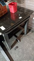 Table top surface showing dark reflective material with scratches and marks. Red plastic container on top for scale.