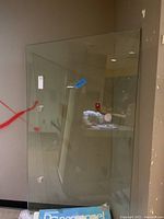 Full view of the large rectangular glass table top leaning upright against a wall. Shows thickness and clear transparency of glass.