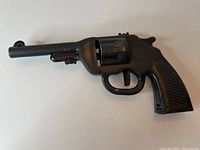 Black metal 1940s style revolver toy cap gun showing side and handle with wear and paint loss visible.