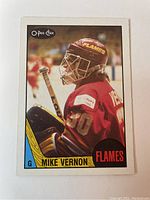 Front side of the 1987 O-Pee-Chee Mike Vernon rookie hockey card showing image of Vernon in goalie gear with Flames branding.