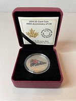 Photo of 2019 Canadian 25-cent coin commemorating 100th anniversary of CN, shown in protective casing inside maroon presentation box with black interior and COA