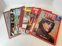 Eight Beatles collector magazines stacked and fanned, visible are various John Lennon covers including Time Magazine.