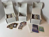 Three open boxes with various sports product cards inside. Loose cards and cards in holders arranged in front of boxes on table.