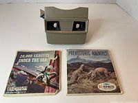 Gray View-Master stereo viewer with two reels in front, '20,000 Leagues Under the Sea' and 'Prehistoric Animals'.