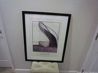 Framed print photo titled 'Grace' shown upright against a wall on a cushioned stool, showcasing the black frame, matte border, and spiral staircase image.
