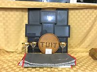 Image showing the entire lot: insulated thermal pizza bag folded, round wooden TUIT sign, three gold rimmed wine glasses, and a black multi-photo picture frame on a checkered beige background.