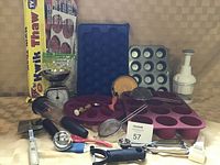 Photo of assorted kitchen tools and bakeware including silicone molds, metal muffin pan, kitchen scale, slap chopper, cookie scoop, and quick thaw film roll