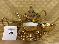 Photo showing the complete Royal Winton Grimwades tea set in reflective gold finish, including teapot, cream pitcher, sugar bowl, one cup and saucer.