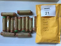 13 rolls of Canadian 1 cent coins wrapped in paper rolls, alongside a yellow envelope with auction label