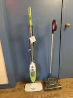 Both the Shark carpet sweeper and the Smart Living Plus wet mop standing upright against a wall on a wooden floor.