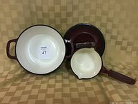 Photo showing the empty casserole pot, saucepan, and their lids displayed on a patterned beige surface.