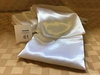 Nine neatly folded white satin chair covers with a smooth, shiny texture displayed on a beige surface.