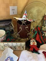 Photo showing various Christmas items including a metal star decoration, metal tree cutout candle holder, holiday mug, penguin ornament, crocheted coaster, and multi-purpose light covers.
