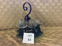 Photo showing six German wine glasses (four matching, two similar) displayed on a black wrought iron stand with a curved handle.