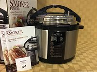 Photo of Emson indoor pressure smoker and cooker unit with digital control panel and lid, alongside user guide and recipes & instructions booklets.