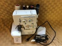 Front and top view of white sewing serger with four spools of thread, power cord, foot pedal, and manual.