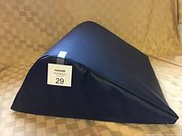 Photo of a black wedge-shaped knee support cushion on a beige checkered fabric background with a Maxsold lot tag labeled '29'.