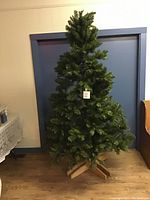 Photo of the 7-foot artificial Christmas tree standing upright with a sturdy homemade wooden stand on a hardwood floor.