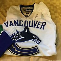 Folded Vancouver Canucks hockey jersey showing chest logo and name, white with blue and green accents, Reebok tag visible