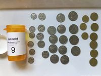 Photo of 33 New Zealand coins laid out in rows alongside an orange pill bottle for scale.