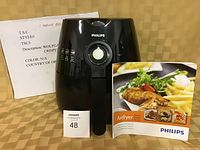 Black Philips air fryer with front manual dial and handle, accompanied by a white sign listing Wolfgang Puck pizza crisper. Includes a MaxSold lot card with number 48 and a Philips Airfryer instruction manual.