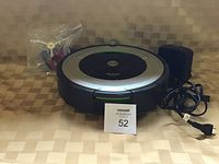 Photo of the Roomba robot vacuum cleaner on a tiled surface, accompanied by its charger with power cord, and a small bag containing an extra filter.