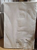 Photo of the bulletin board wrapped in protective plastic, showing the front cork surface and oak finish frame edges.