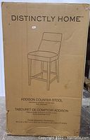 Cardboard packaging for Distinctly Home Addison Counter Stool showing product illustration, product name, dimensions, and materials.