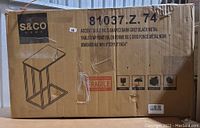 Original product cardboard packaging for Safdie & Co. Accent Table, showing model number 81037.Z.74, product name, and shipping symbols with fragile and orientation icons.