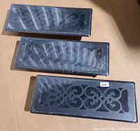 Three rectangular black vent covers with decorative cut-out patterns in original packaging, shown from top angle on cardboard surface.