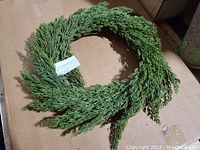 Full view of circular green cypress wreath on cardboard background.