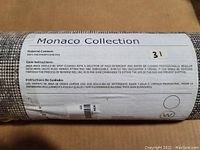 Label on rolled area rug showing Monaco Collection, material content as 100% polypropylene pile, care instructions in English and Spanish.