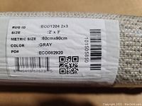 Close-up photo of the label on the rug showing size as 2' x 3', color grey, and product ID ECO1204.