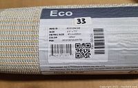 Close-up photo of the product label showing size, color, material, and origin details for the Deerwood flatweave rug.