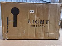 Cardboard box showing Light Society branding, product is inside box, likely the black Sena wall sconce in marble as described