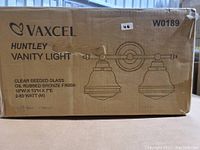 Box labeled Vaxcel Huntley Vanity Light with product specifications and illustration of the 2-light fixture.