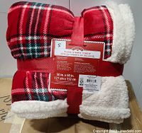 Red plaid and white sherpa throw blanket folded and tied with red ribbon showing packaging label