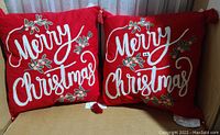 Two red holiday decorative pillows with "Merry Christmas" embroidered text and green leaf accents, displayed side by side.