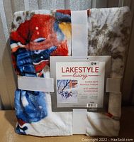 Folded Lakestyle Living super soft printed throw with white securing bands, showing part of printed design in red, blue, and brown.