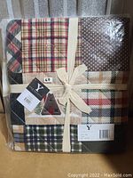 Packaged throw blanket tied with cream-colored ribbon, showcasing patchwork plaid and polka dot patterns with multiple tags visible.