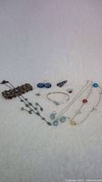 Overall photo showing multiple pieces of blue jewelry including necklaces, bracelet, earrings, and a ring arranged on white cloth.