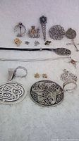 Overview photo of all items in the lot displayed on white fabric including various pins, pendants, earrings, and rings with Celtic designs