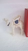 Camel figurine standing upright next to its red box on a white backdrop, showing overall shape and size.
