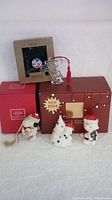 Photo showing all three items together with their respective branded boxes: Lenox Snoopy salt and pepper set, Lenox Snoopy holiday nest ornament, and Marquis Waterford crystal Snoopy ornament in red box.