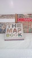 Overview photo of three hardcover map books arranged together on white surface including Great Maps, Great City Maps, and The Map Book.