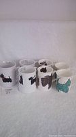 Seven mugs with Scottie dogs and one motorcycle design arranged on a white surface for lot display.